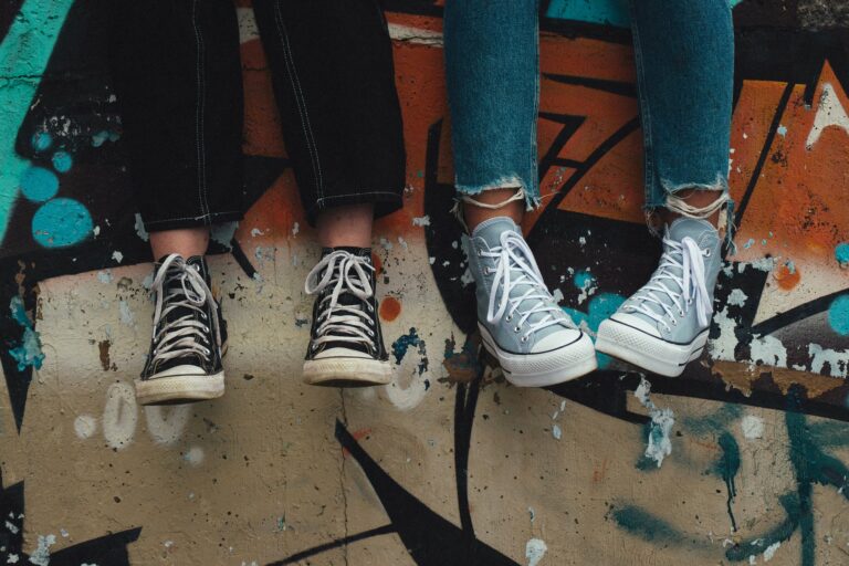 Deux adolescents assis sur un mur peint, dont on ne voit que les baskets