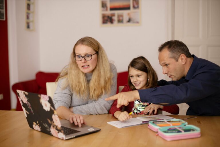 Deux parents et une enfant autour d'un cahier et d'un ordinateur, à la table familiale